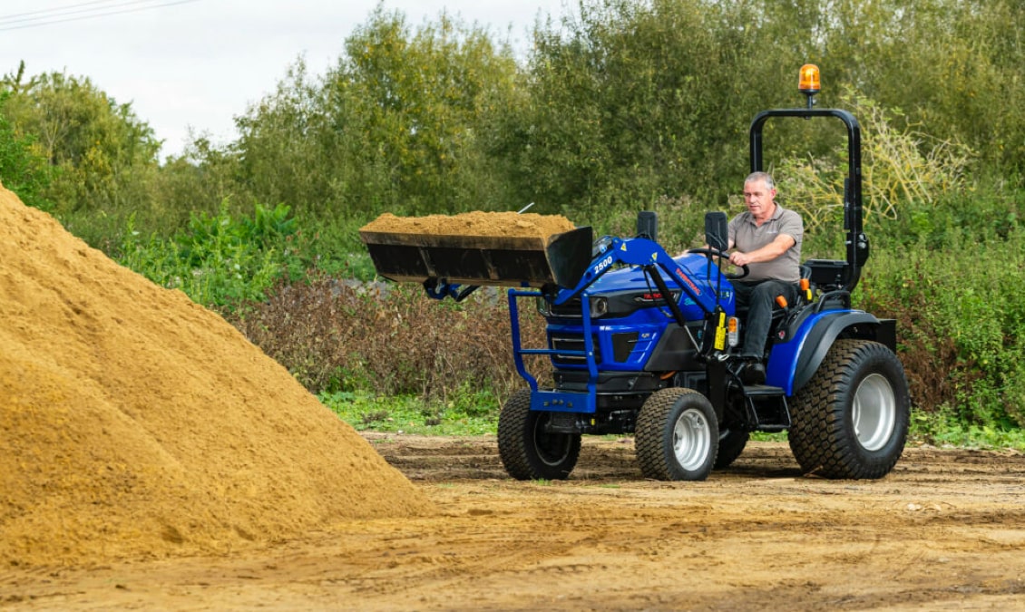 A Farmtrac FT25G tractor moving sand in its front loader.