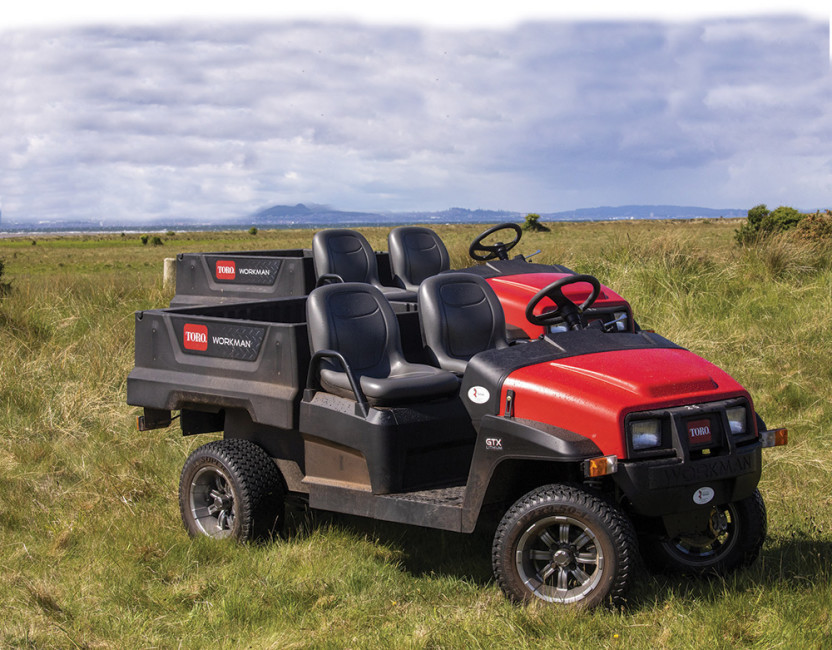 Two Toro Workman vehicles, one in front of the other in a field.